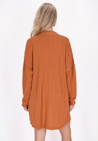 Abito oversize a maniche lunghe in tessuto testurizzato color arancio bruciato. Presenta un collo rotondo e un orlo leggermente curvo con una vestibilità comoda.
