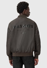 Brun bomberjakke med et blankt sort "ALLSAINTS" logo på ryggen, med ribbet krave og elastisk kant og manchetter.