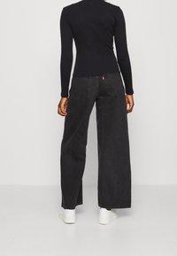 Svarta jeans i vid modell med hög midja, bakfickor och röd logodetalj. Styla med en åtsittande långärmad svart topp och vita sneakers.