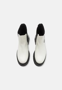 Botine albe până la gleznă, cu un finisaj lucios, panouri elastice laterale negre și o talpă rugged neagră. Prezintă un design elegant și minimalist.
