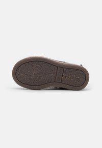 Semelle de chaussure en caoutchouc marron avec une surface texturée, une forme incurvée et un design à motifs subtils. notable pour ses accents en matériaux naturels.