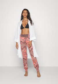 Svart bikini topp, hvit åpen skjorte og mønstrede bukser med korall- og paisleymønster. Mykt stoff, løs passform og ankelmanchetter.