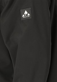 Schwarze Jacke aus glattem Stoff mit einem quadratischen Logopatch, das weiße Berggrafiken und den Text "WHISTLER" zeigt.