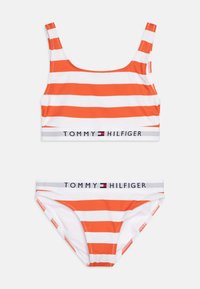 Nabor bikini z oranžno-belo črtasto zasnovo, ki vključuje športni zgornji del in ustrezne spodnje delce, s sivo logotipno elastiko na kateri je napis "TOMMY HILFIGER".