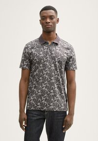 Polo de manga corta en gris oscuro con un patrón de hojas. Presenta un cuello con solapa y una tela texturizada. Se lleva con jeans oscuros.