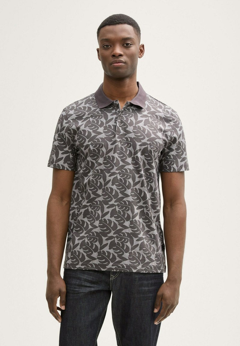 Polo de manga corta en gris oscuro con un patrón de hojas. Presenta un cuello con solapa y una tela texturizada. Se lleva con jeans oscuros.