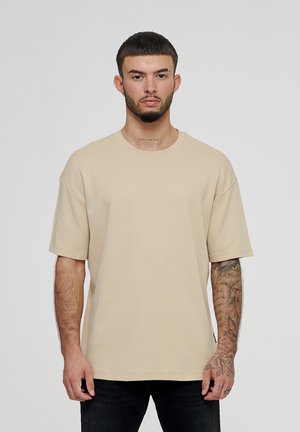 Beige oversized T-shirt lavet af bomuld, med korte ærmer, rund hals og lige kant. Ingen synlige mønstre eller hardware.