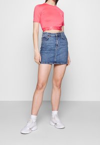 Růžové cropped tričko s logem, kombinované s modrou džínsovou sukní. Model má na sobě bílé sportovní boty a ponožky do poloviny lýtek.