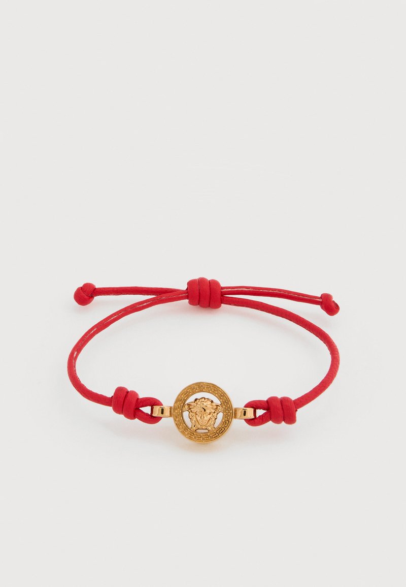 Rødt snorarmbånd med en rund gullmedaljong med løvehode-design, flankert av gullaksenter og festet med justerbare knuter.