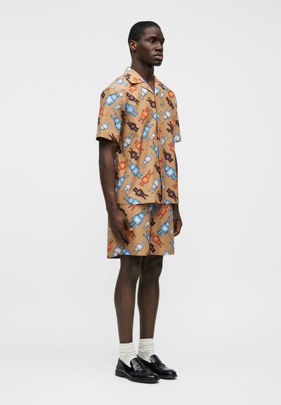 Ensemble composé d'une chemise à manches courtes et d'un short marron avec un motif ludique de personnages de dessins animés en bleu, orange et noir. Tissu lisse, coupe décontractée.