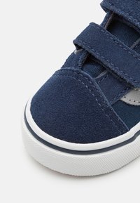 Marinblå mockasneaker med två kardborrband, en strukturerad vit gummisula och en slät blå tygpanel.