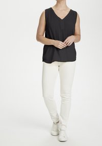 Haut noir sans manches avec un col en V et des boutons sur le devant, associé à un jean blanc slim et des baskets blanches. Texture de tissu lisse.