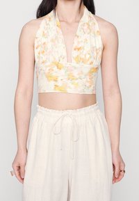Blommönstrad halterneck crop top i mjukt tyg, med djup halsringning och figurnära midja i ljusa färger. Kombinerad med lösa beige byxor.