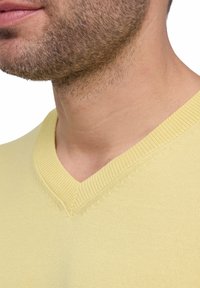 Maglione a V in un giallo chiaro, caratterizzato da un motivo a maglia testurizzato e colletto a costine. Inquadratura ravvicinata del colletto e dell'area del collo.