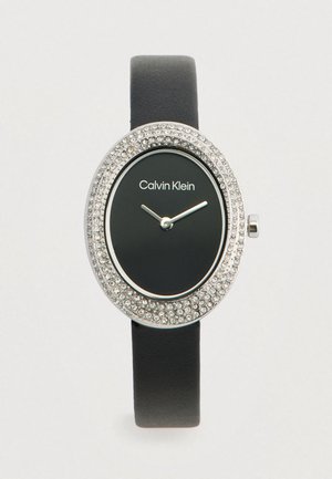 Orologio con cinturino in pelle nera, con cassa ovale in metallo argentato impreziosita da cristalli trasparenti, che presenta un quadrante nero e indici delle ore bianchi.