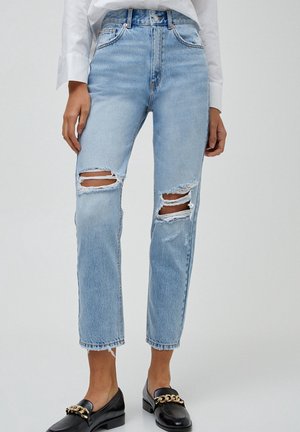 Helleblaue hoch taillierte Jeans mit ausgefransten Stellen an den Knien, geradem Schnitt und fransigen Säumen. Kombiniert mit schwarzen Mokassins.