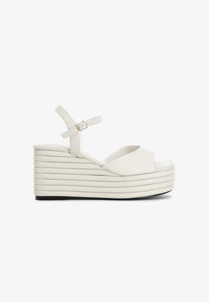 White platform wedge sandals featuring a smooth upper, open toe design, adjustable ankle strap, and stacked ridged sole.
