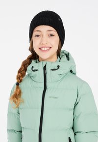 Helle grüne Pufferjacke mit Reißverschluss und schwarzen Akzenten, kombiniert mit einer schwarzen, gerippten Strickmütze. Verfügt über eine Kapuze und ein Markenlogo.