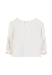 Długosłaby, kremowy top z okrągłym dekoltem i różowymi falbankami na mankietach oraz dekolcie. Posiada zapięcie na trzy guziki z tyłu.