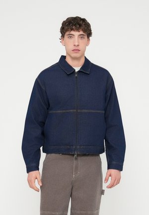 Σκούρο μπλε τζιν μπουφάν με γιακά, μπροστινό φερμουάρ και εμφανείς ραφές. Χαλαρή γραμμή και κοντή σχεδίαση, συνδυασμένα με γκρι παντελόνια.