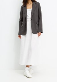 Blazer gris à revers, deux poches avant, associé à une robe blanche sans bretelles et des baskets blanches, mettant en avant un look moderne et superposé.