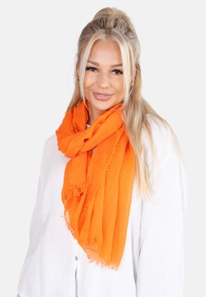 Écharpe orange vif en tissu texturé, drapée délicatement autour du cou avec des bords frangés, portée sur une chemise blanche.