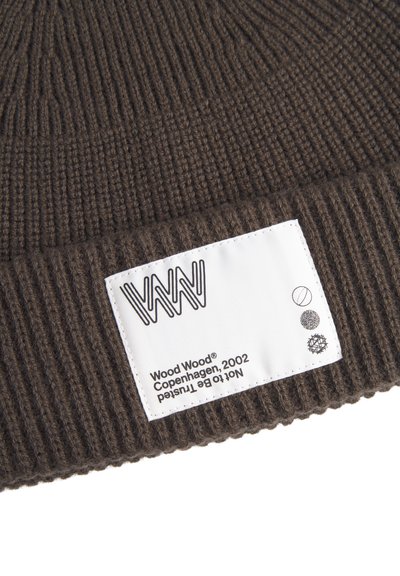 Ruda megzta beanie kepurė su briaunuota tekstūra ir stačiakampiu baltu žymenčiu, kuriame yra prekės ženklas ir priežiūros simboliai.