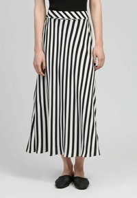 Jupe maxi à rayures noires et blanches en tissu léger, dotée d'une taille ajustée et d'une forme évasée. Chaussures noires à enfiler.