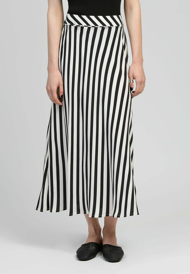 Jupe maxi à rayures noires et blanches en tissu léger, dotée d'une taille ajustée et d'une forme évasée. Chaussures noires à enfiler.