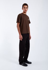 Brown cotton t-shirt with a round neckline and short sleeves, paired with black corduroy pants and black loafers.