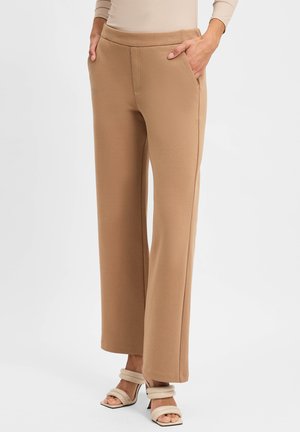 Beige Strick-Hose mit weitem Bein und glatter Textur, ausgestattet mit Seitentaschen und einem Bund. Kombiniert mit hellen, hohen Sandalen.