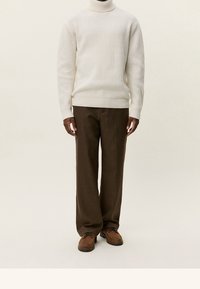 Pull à col roulé côtelé crème, pantalon large à carreaux marron, et chaussures marron à lacets. Coupe structurée, texture douce, et design confortable.