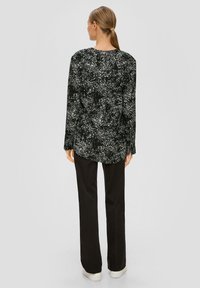 Zwarte shirt met een wit gespikkeld patroon, lange mouwen en een relaxte pasvorm. Gecombineerd met zwarte broek en witte sneakers. Gladde textuur.
