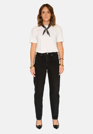 Jean noir taille haute associé à un t-shirt blanc. Une écharpe noire nouée autour du cou. Élégantes talons noirs. Tissu lisse et coupe ajustée.