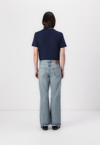 Tamno plavi majica kratkih rukava u kombinaciji s svijetloplavim trapericama s flared krojem, na kojima se nalazi smeđa kožna oznaka na pojasu i tamna obuća.