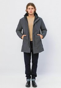Grijze waterdichte jas met een capuchon, voorzijde rits, en twee zijzakken, gedragen over een beige trui en donkere spijkerbroek; gladde textuur.