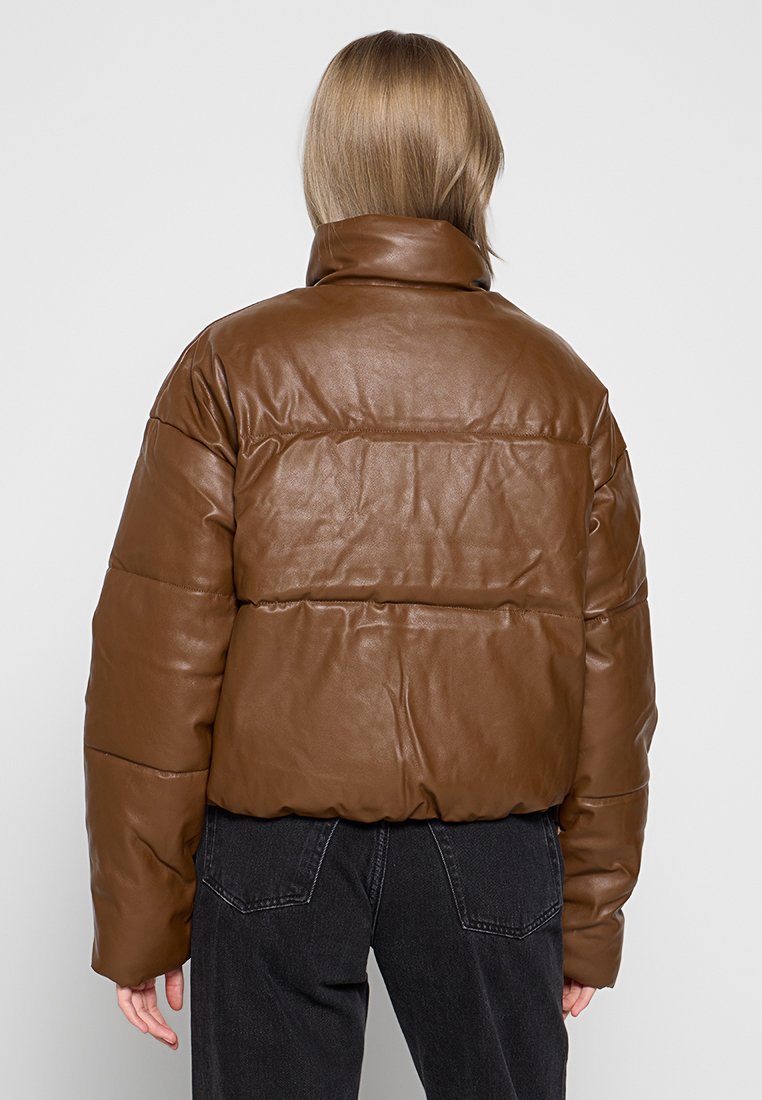 Brązowa kurtka puchowa z ekologicznej skóry z wysokim kołnierzem, pikowanym wzorem i skróconym krojem, widok z tyłu z czarnymi dżinsami.