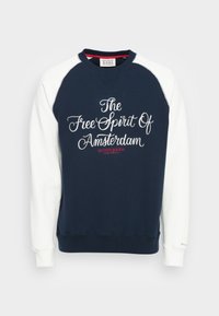 Dunkelblaues Sweatshirt mit weißen Raglanärmeln. Beinhaltet gestickten Text: "Der Freigeist von Amsterdam" in Kursivschrift, mit einem roten Akzent.