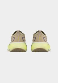 Ζεύγος μπεζ και κίτρινων παπουτσιών Nike για τρέξιμο, εμφανιζόμενα από πίσω, με χοντρές κίτρινες σόλες και το λογότυπο Supernova στις ταμπέλες της φτέρνας.