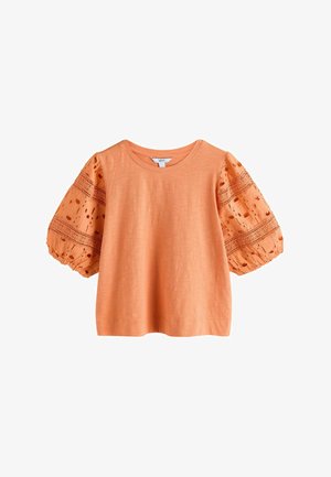 Lühike oranž kampsunist topp õhuliselt tikandiga varrukatega ja ümmarguse kaelusega, mida tähistab "Next".