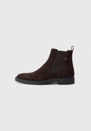 Mørkebrun nubuck Chelsea-støvle med elastiske sidedele, rund tå og sort gummisål. Har en trækflap for nem påtagning.