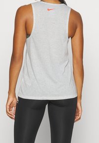 Graues Mesh-Trägershirt mit rundem Ausschnitt und Racerback-Design, mit einem kleinen roten Nike-Logo am oberen Rücken. Schwarze Leggings werden getragen.