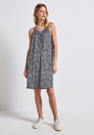 Navy and cream sleeveless dress with a leaf print, flowing silhouette, and gathered neckline, paired with white sneakers.