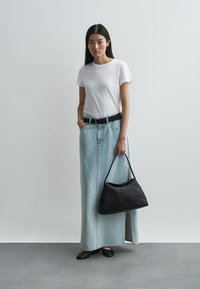 Valkoinen t-paita, vaaleansininen farkku-maksihame, musta vyö, musta kudottu käsilaukku. Henkilö, joka käyttää mustia tasapohjaisia kenkiä, seisoo neutraalilla taustalla.