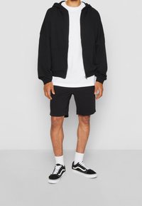 Sweat à capuche noir zippé, t-shirt blanc, short noir, baskets noires et blanches. Manches courtes, coupe décontractée, tissu doux, design minimaliste.