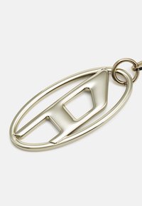 Metallnyckelring i oval form med geometrisk utskärning i en polerad guldfinish. Slät yta med glänsande ytor.