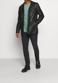 Svart läderjacka med klassisk krage, bärs över en teal t-shirt. Mörka byxor och svarta klackstövlar fulländar outfiten.