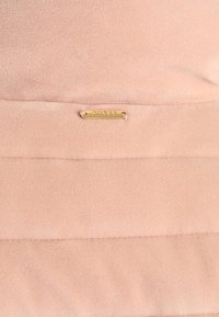 Różowy polarowy materiał o gładkiej fakturze, z małą złotą metalową metką z wytłoczonym napisem "GUESS".