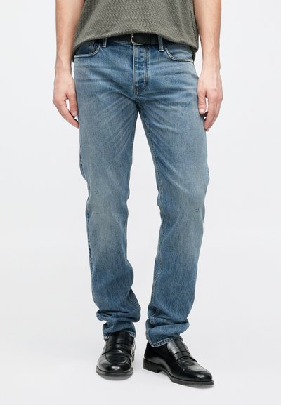 Τζιν παντελόνια ελαφρώς μπλε με ίσια γραμμή, διαθέτουν κλασικό σχεδιασμό με πέντε τσέπες και διακριτική ξεθώριασμα, συνδυασμένα με μαύρα δερμάτινα παπούτσια.