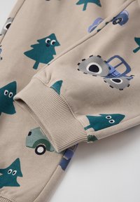 Lys brune sweatpants med grønne træer og legende grafikker af køretøjer og øjne. Ribbet kant og blød bomuldsblandingsstruktur.